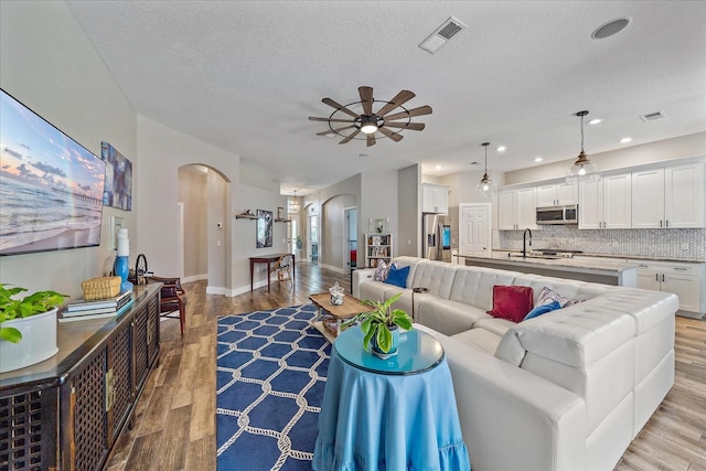 living room with a textured ceiling, light wood-type flooring, ceiling fan, and sink