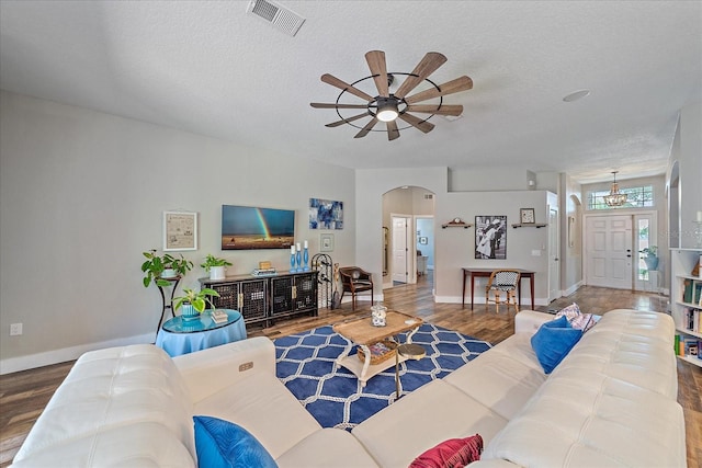 living room with ceiling fan with notable chandelier, wood-type flooring, and a textured ceiling