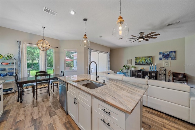 kitchen featuring light stone countertops, sink, hanging light fixtures, an island with sink, and white cabinets