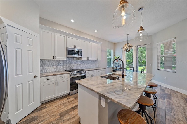 kitchen featuring white cabinets, sink, appliances with stainless steel finishes, and an island with sink