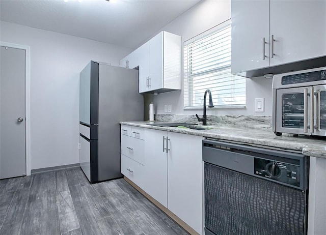 kitchen featuring white cabinetry, stainless steel refrigerator, dishwasher, light stone countertops, and hardwood / wood-style floors