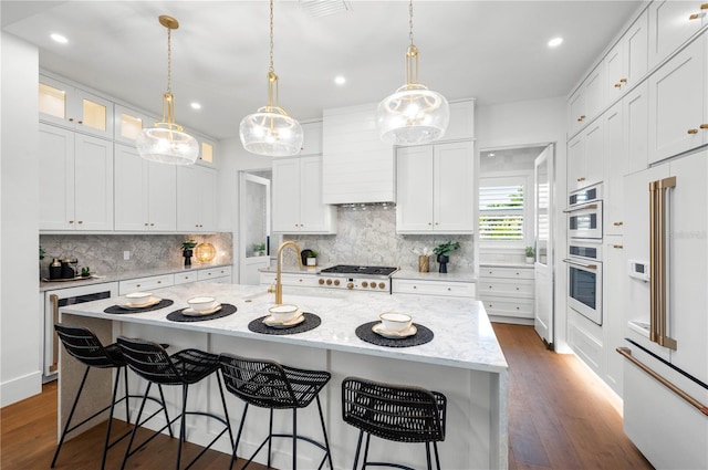 kitchen featuring white cabinets, a center island with sink, built in fridge, wine cooler, and light stone countertops