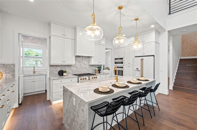 kitchen featuring white cabinets, light stone countertops, white fridge with ice dispenser, and an island with sink