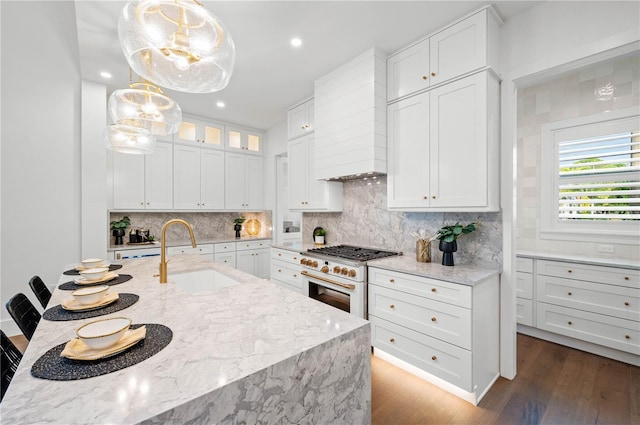 kitchen featuring high end range, light stone countertops, sink, decorative light fixtures, and white cabinetry