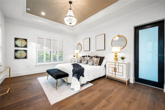 bedroom featuring a tray ceiling, a chandelier, dark wood-type flooring, and ornamental molding