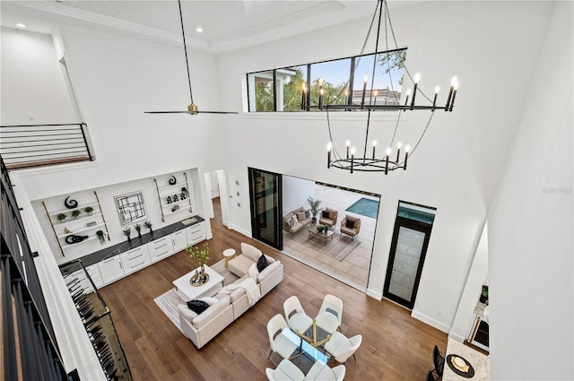 living room with a raised ceiling, a towering ceiling, wood-type flooring, and ceiling fan with notable chandelier