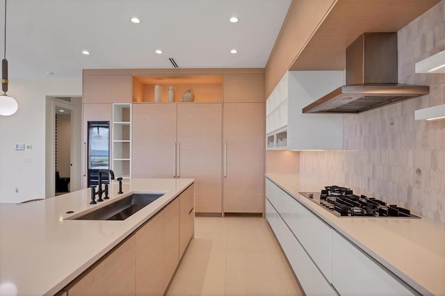 kitchen with decorative light fixtures, wall chimney range hood, sink, gas stovetop, and light tile patterned floors