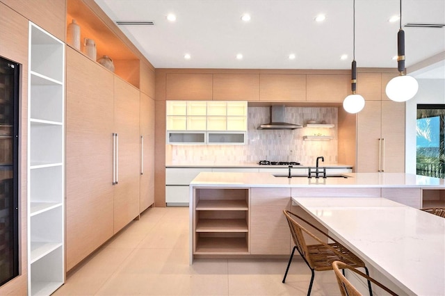 kitchen with pendant lighting, wall chimney range hood, decorative backsplash, sink, and light tile patterned floors