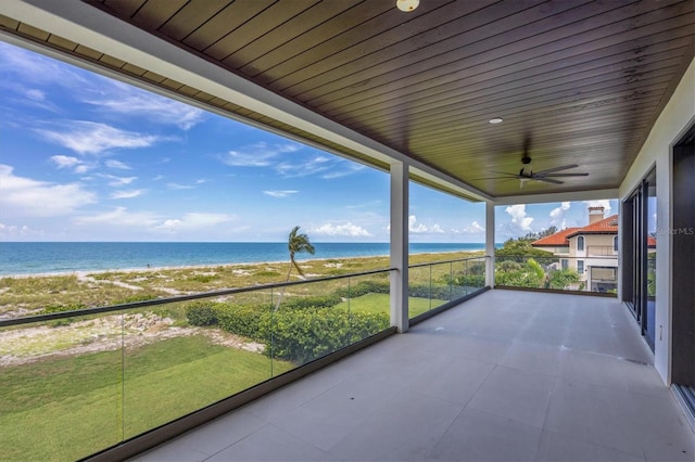 unfurnished sunroom featuring ceiling fan, a water view, a beach view, and wooden ceiling