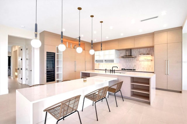 kitchen featuring tasteful backsplash, decorative light fixtures, wall chimney range hood, a large island with sink, and sink