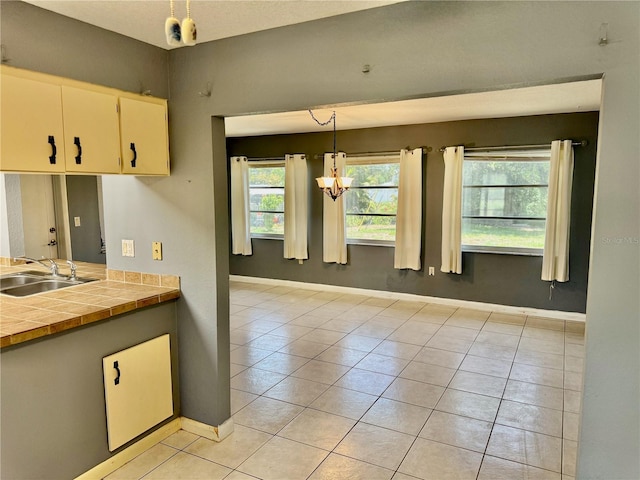 kitchen featuring light tile patterned floors, an inviting chandelier, white cabinets, decorative light fixtures, and sink