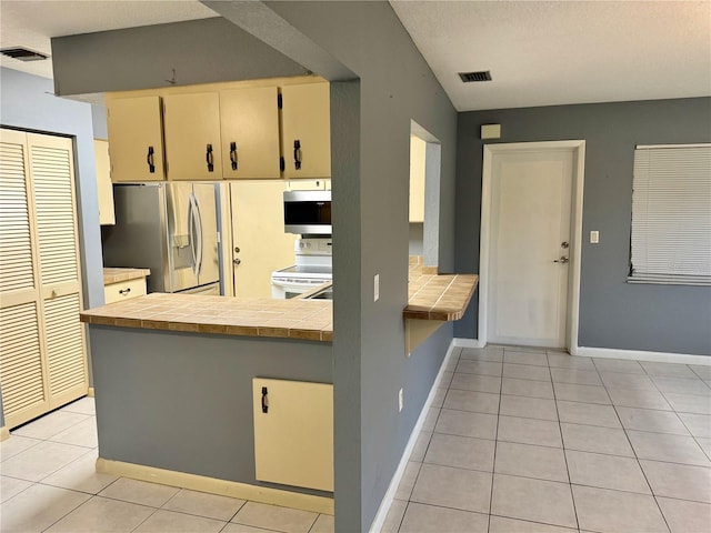 kitchen featuring appliances with stainless steel finishes, white cabinets, kitchen peninsula, light tile patterned floors, and tile countertops