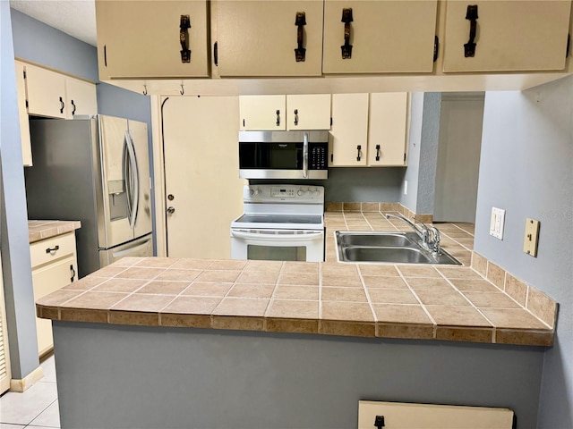 kitchen with tile counters, light tile patterned floors, kitchen peninsula, appliances with stainless steel finishes, and sink