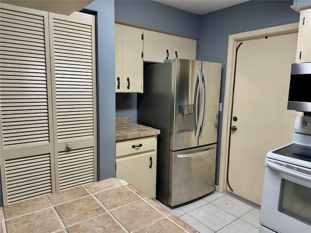 kitchen featuring white range with electric stovetop, tile countertops, stainless steel fridge, and light tile patterned floors