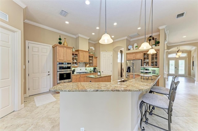 kitchen featuring crown molding, light stone counters, appliances with stainless steel finishes, decorative light fixtures, and a large island with sink