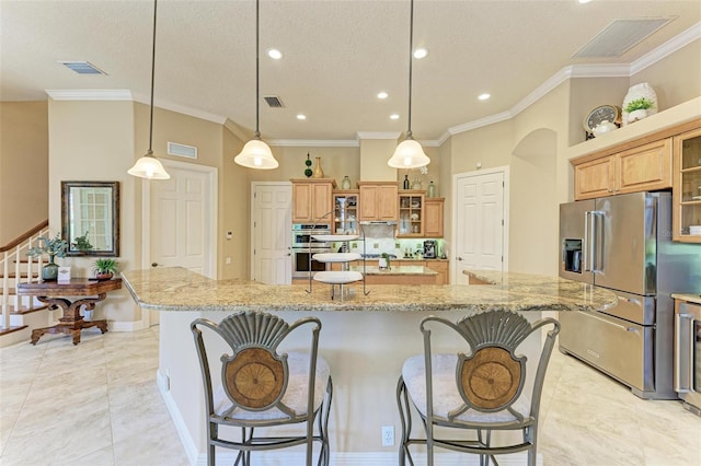 kitchen with crown molding, hanging light fixtures, appliances with stainless steel finishes, a kitchen breakfast bar, and a large island with sink