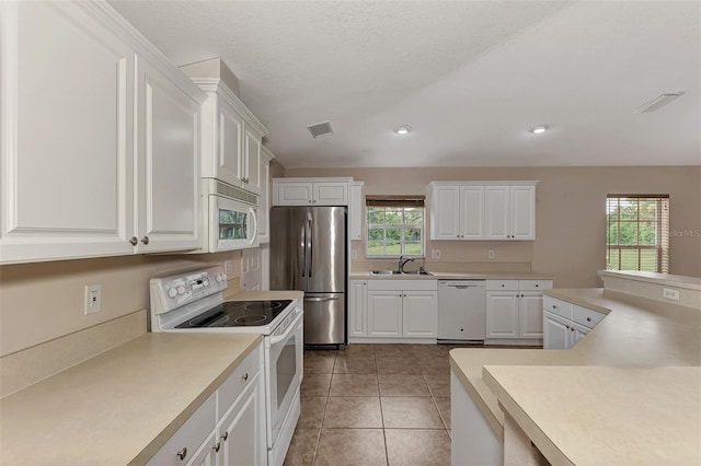 kitchen with sink, light tile patterned floors, white appliances, a textured ceiling, and white cabinets