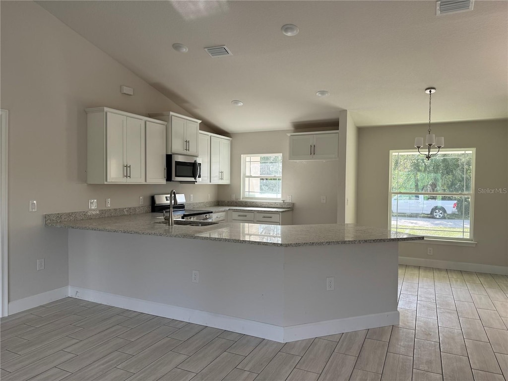 kitchen with white cabinetry, kitchen peninsula, appliances with stainless steel finishes, decorative light fixtures, and light hardwood / wood-style flooring