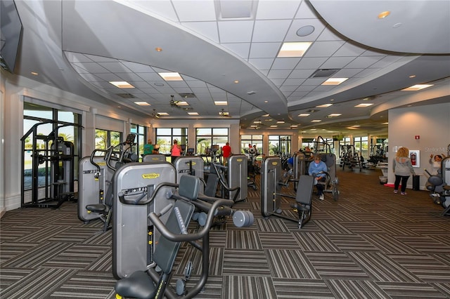 gym with a paneled ceiling and dark colored carpet