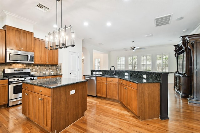 kitchen with ceiling fan with notable chandelier, stainless steel appliances, light hardwood / wood-style flooring, a kitchen island, and hanging light fixtures