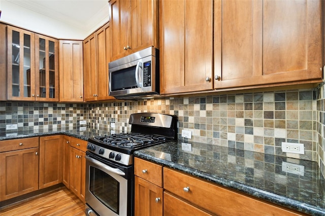 kitchen featuring backsplash, dark stone countertops, crown molding, and appliances with stainless steel finishes