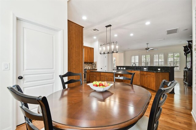 dining room with ceiling fan with notable chandelier, sink, and light hardwood / wood-style flooring