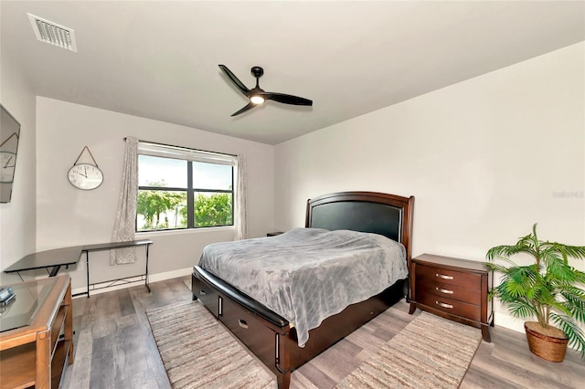 bedroom with ceiling fan, visible vents, baseboards, and wood finished floors