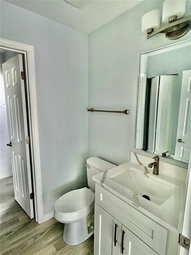 half bathroom featuring vanity, toilet, and wood finished floors