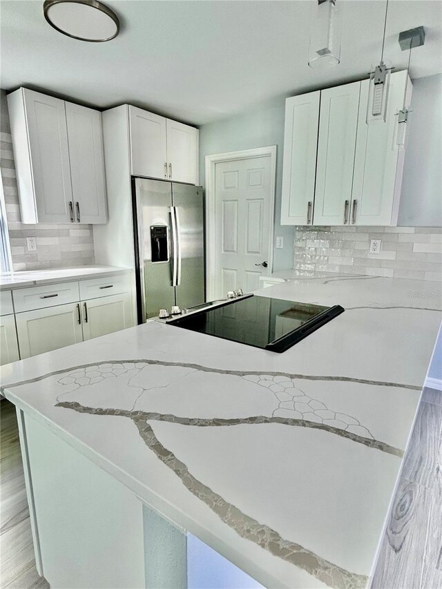 kitchen with hanging light fixtures, decorative backsplash, white cabinets, light stone countertops, and stainless steel fridge with ice dispenser