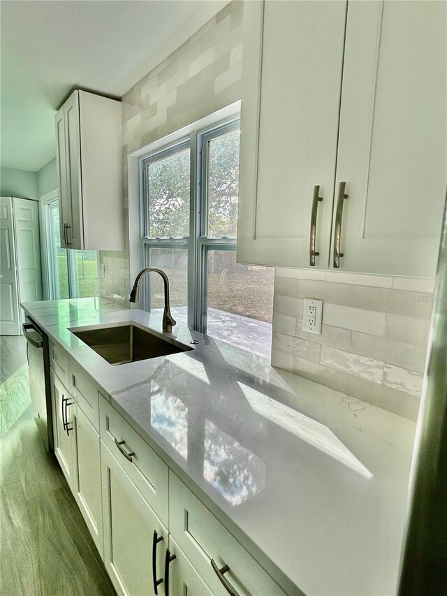 kitchen featuring light stone counters, tasteful backsplash, white cabinetry, a sink, and dishwasher