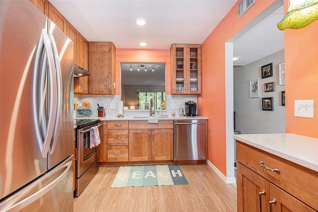 kitchen featuring light stone countertops, stainless steel appliances, light hardwood / wood-style floors, rail lighting, and backsplash