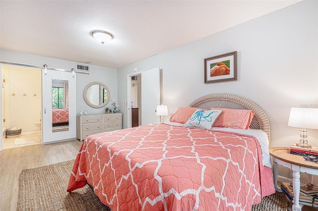 bedroom with connected bathroom, a textured ceiling, a barn door, and light hardwood / wood-style flooring