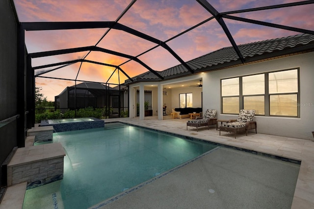 pool at dusk with outdoor lounge area, ceiling fan, a lanai, and an in ground hot tub