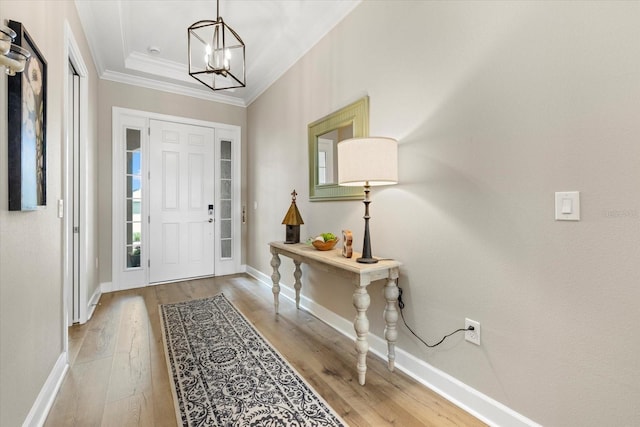 foyer entrance featuring a raised ceiling, crown molding, an inviting chandelier, and light wood-type flooring