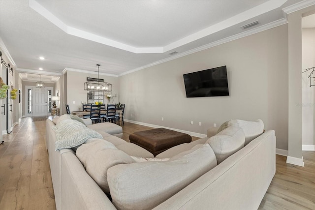 living room with a raised ceiling, crown molding, light hardwood / wood-style floors, and an inviting chandelier