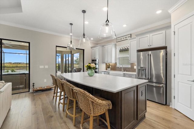 kitchen with a kitchen breakfast bar, hanging light fixtures, light wood-type flooring, appliances with stainless steel finishes, and a kitchen island