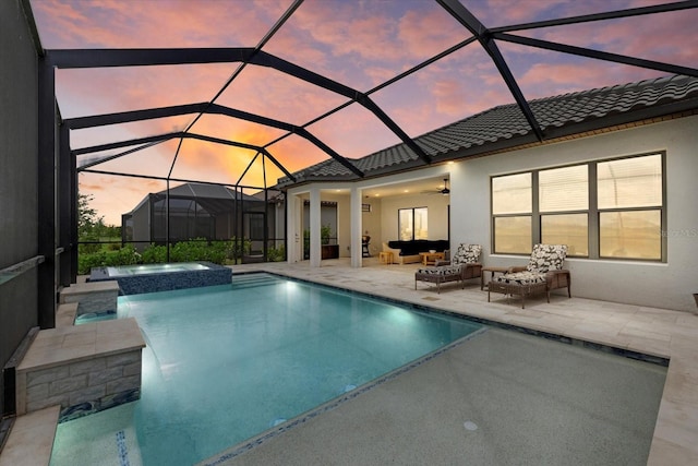 pool at dusk with outdoor lounge area, ceiling fan, glass enclosure, an in ground hot tub, and a patio