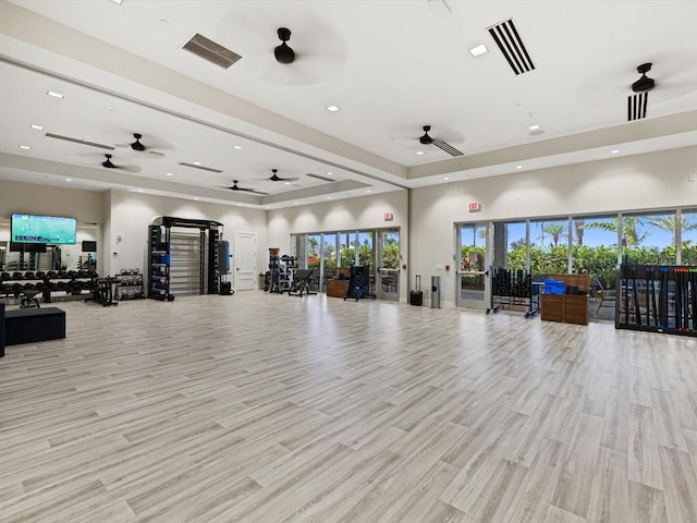 gym featuring ceiling fan, light hardwood / wood-style floors, a raised ceiling, and a towering ceiling