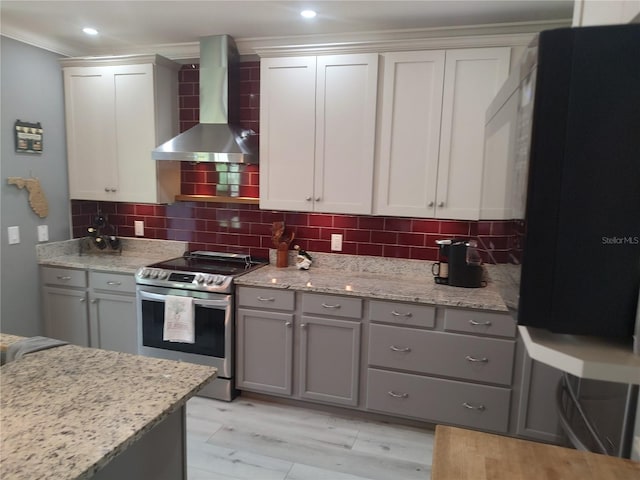 kitchen with light hardwood / wood-style flooring, stainless steel electric range oven, wall chimney range hood, and decorative backsplash