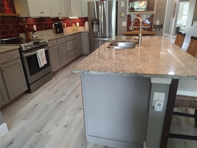 kitchen with appliances with stainless steel finishes, a breakfast bar, light hardwood / wood-style flooring, a kitchen island with sink, and sink