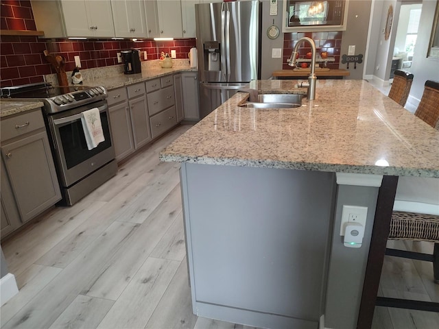 kitchen featuring sink, appliances with stainless steel finishes, light stone countertops, an island with sink, and a kitchen bar