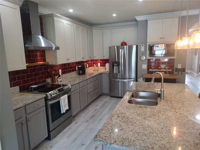 kitchen featuring ornamental molding, appliances with stainless steel finishes, light hardwood / wood-style floors, and wall chimney range hood