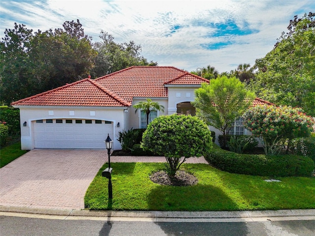 mediterranean / spanish house with a tile roof, a front yard, stucco siding, decorative driveway, and an attached garage