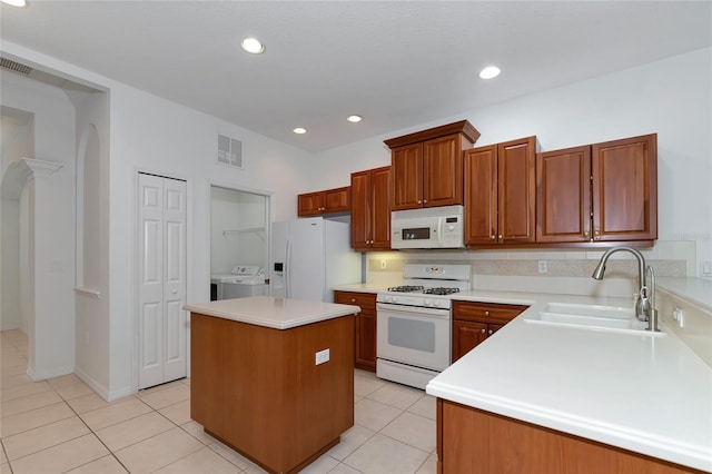 kitchen featuring a sink, a kitchen island, white appliances, light tile patterned floors, and washing machine and clothes dryer