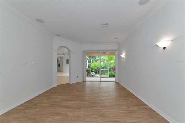 empty room with crown molding, light wood-style floors, visible vents, and baseboards