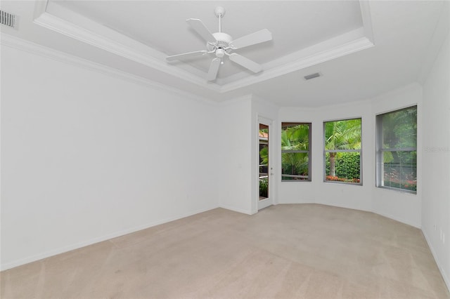 unfurnished room featuring a raised ceiling, ornamental molding, visible vents, and light carpet