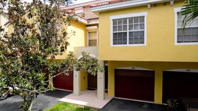 view of front of home featuring an attached garage, driveway, a tile roof, and stucco siding