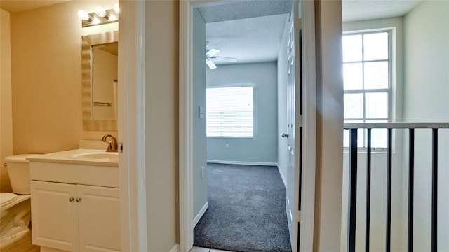 half bath featuring baseboards, a textured ceiling, toilet, and vanity