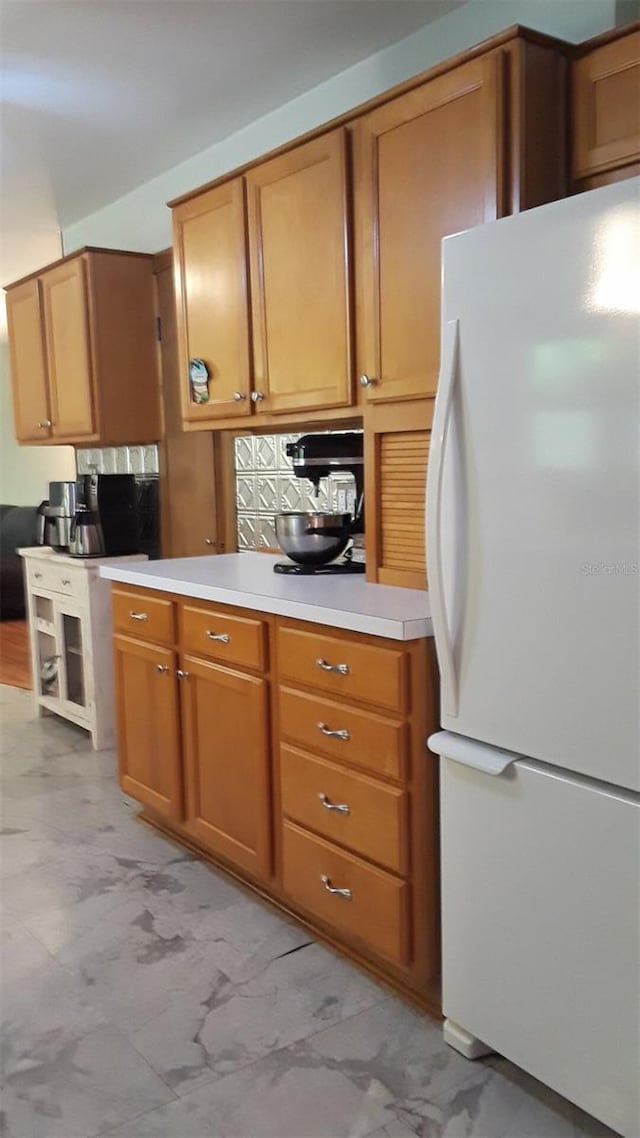 kitchen with light countertops, freestanding refrigerator, and brown cabinets