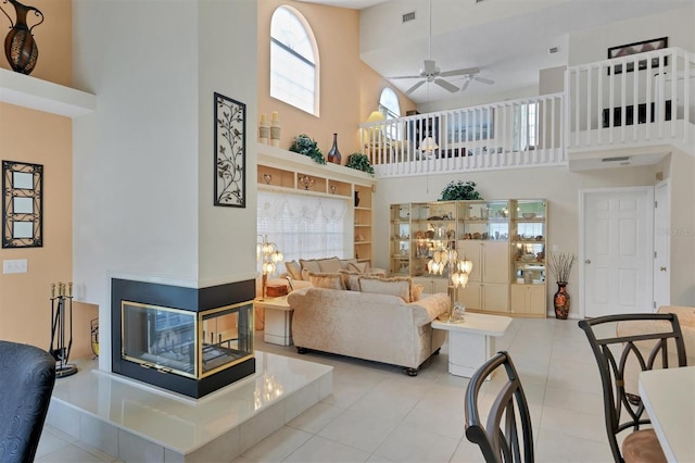 living room with a high ceiling, a multi sided fireplace, ceiling fan, and light tile patterned floors